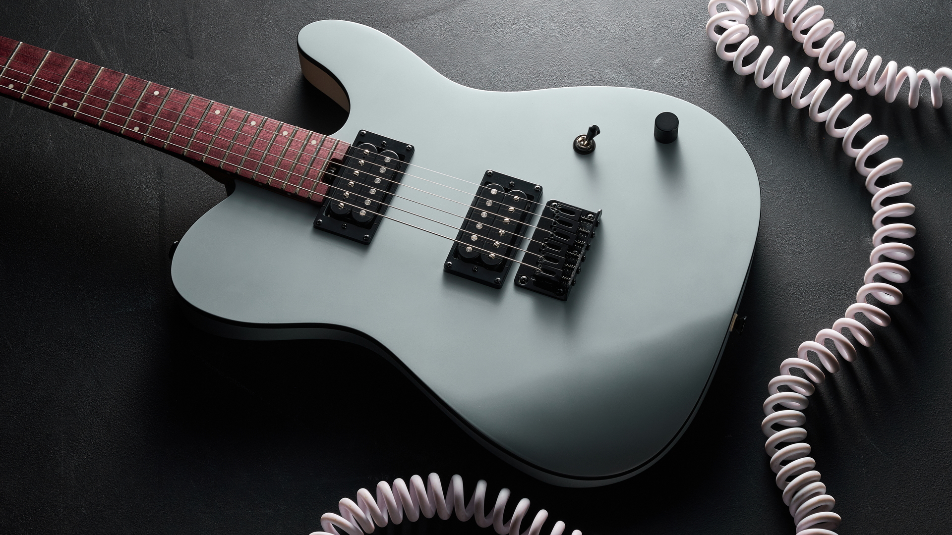 A Charvel Standard Series San Dimas Style 2 SD2 HH HT lying on a dark floor with a coiled guitar cable