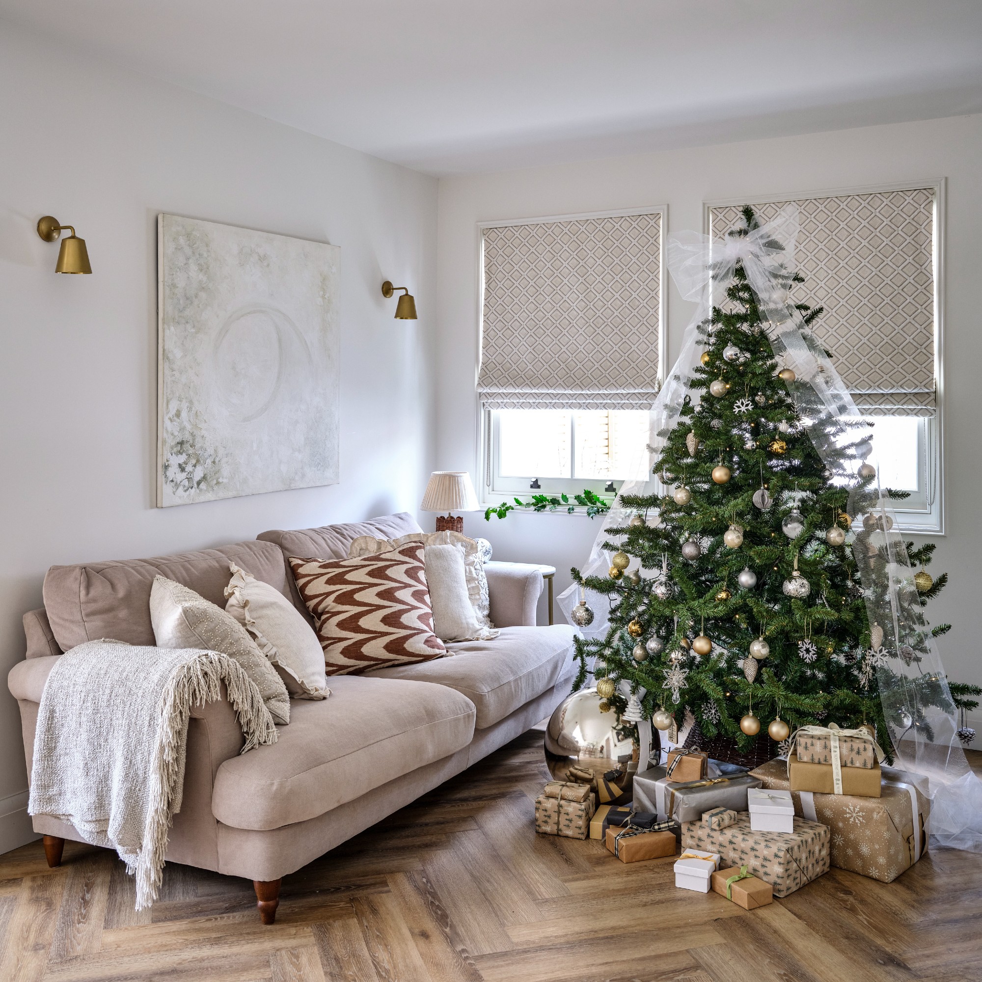 A living room with a neutral sofa and a decorated Christmas tree with a large white organza bow