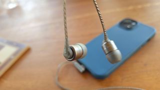 SoundMagic E80D wired in-ear headphones dangling above blue smartphone