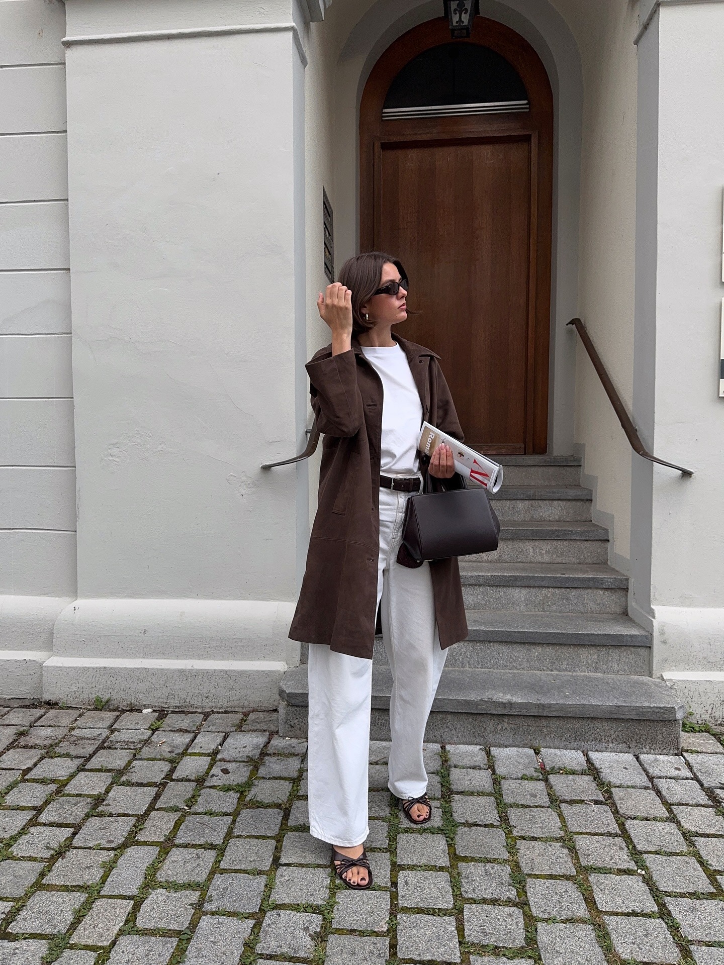 Influencer @maryljean wears white jeans with brown heels, a white-shirt and a brown knee-length jacket.