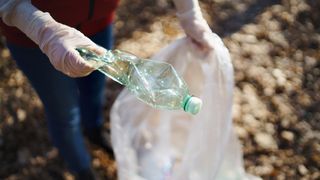 Woman picking up waste plastic water bottle