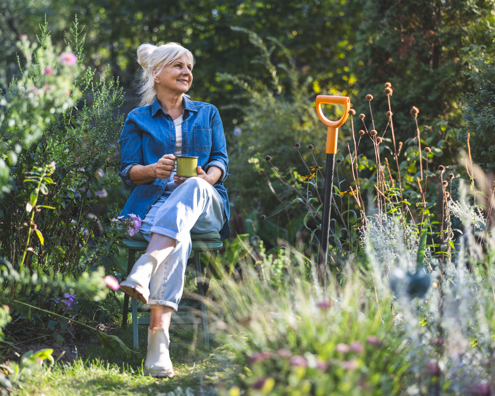 Woman sitting on a chair with a cup or tea in the garden, relaxing after gardening