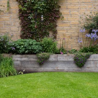 Garden with raised wooden flower beds backing onto brick wall