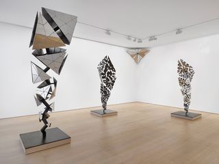 Three sculptures consisting of geometric shapes on a frame, stand in a white gallery