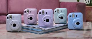 The Fujifilm Instax Mini 12 on a table with each of its five color choice