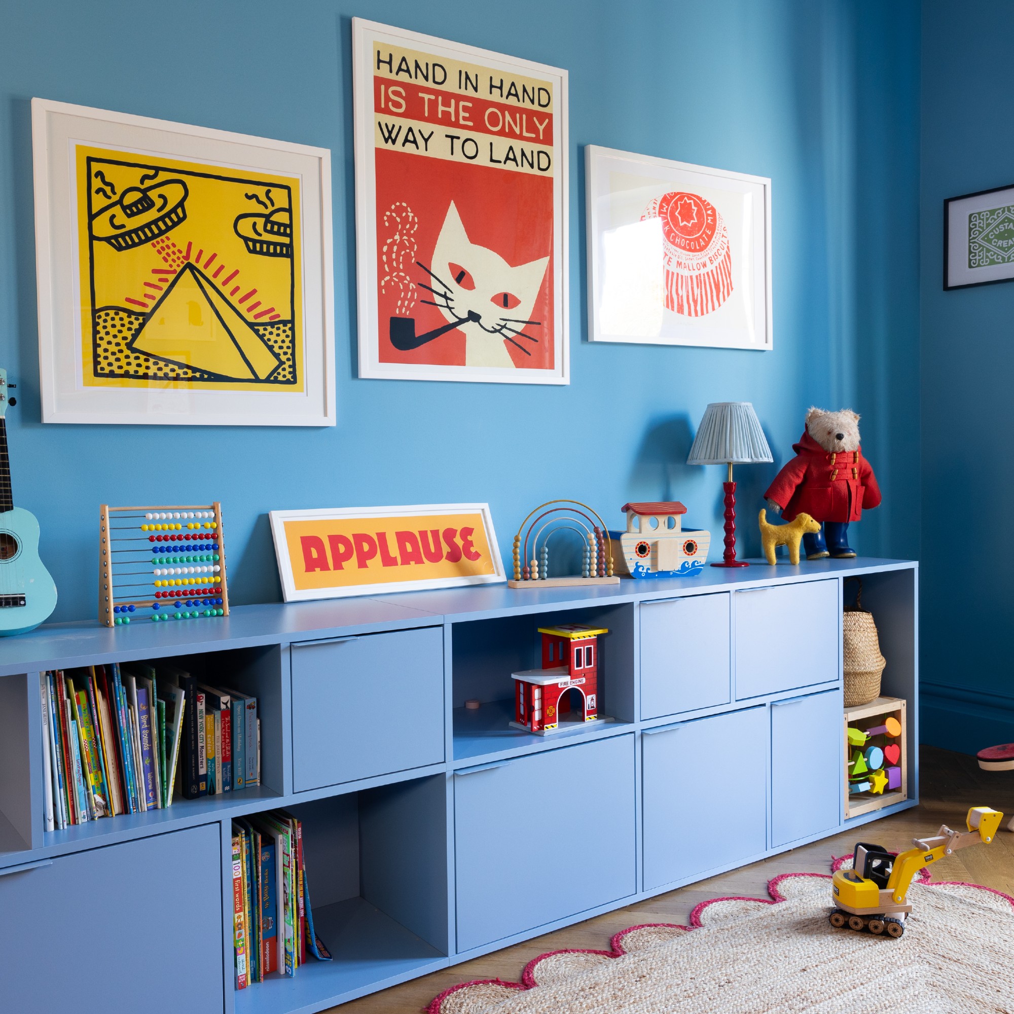 A blue living room with a tonal toy storage unit and a scalloped jute rug on the floor
