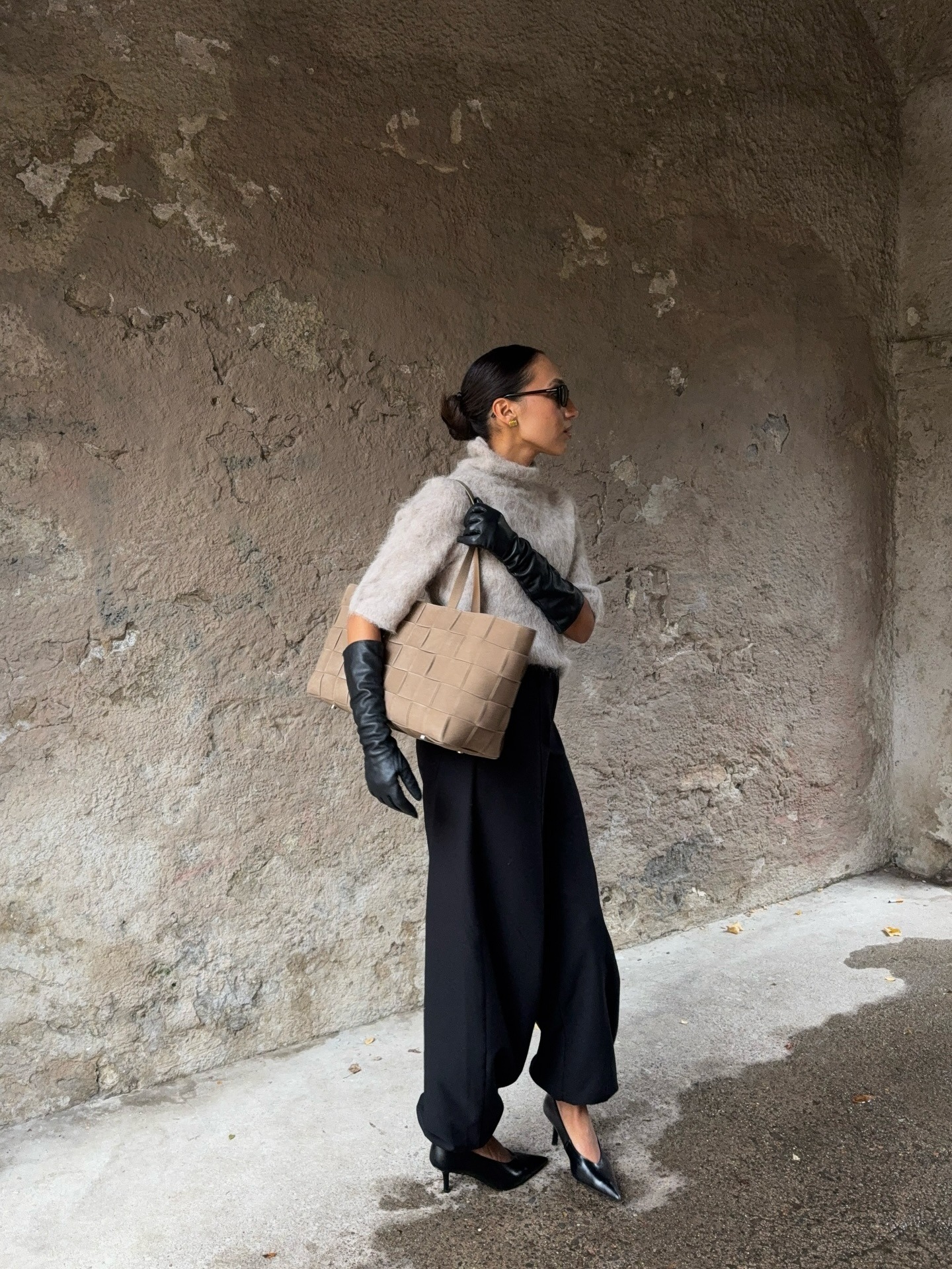 Woman wears grey top, black trousers and suede bag