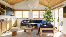 modern coastal style living room with a wooden panelled ceiling and large paper rice ceiling glob lampshade and navy sofa with topper