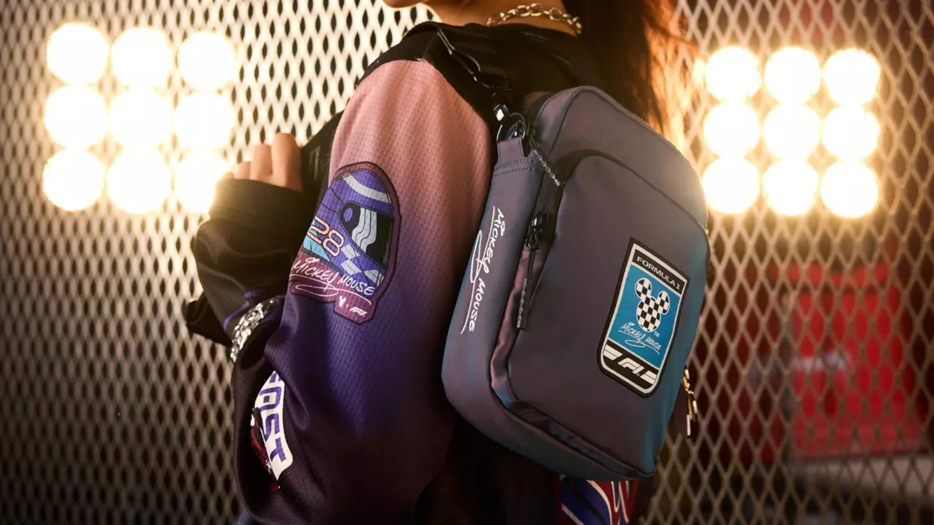 A woman holds a Disney F1 crossbody bag against a background with racing lights shining brightly