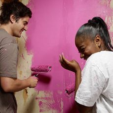 Two people painting a wall pink while laughing