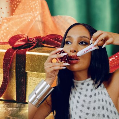 a golden gift package with a red ribbon next to a woman with dark hair and silver jewelry