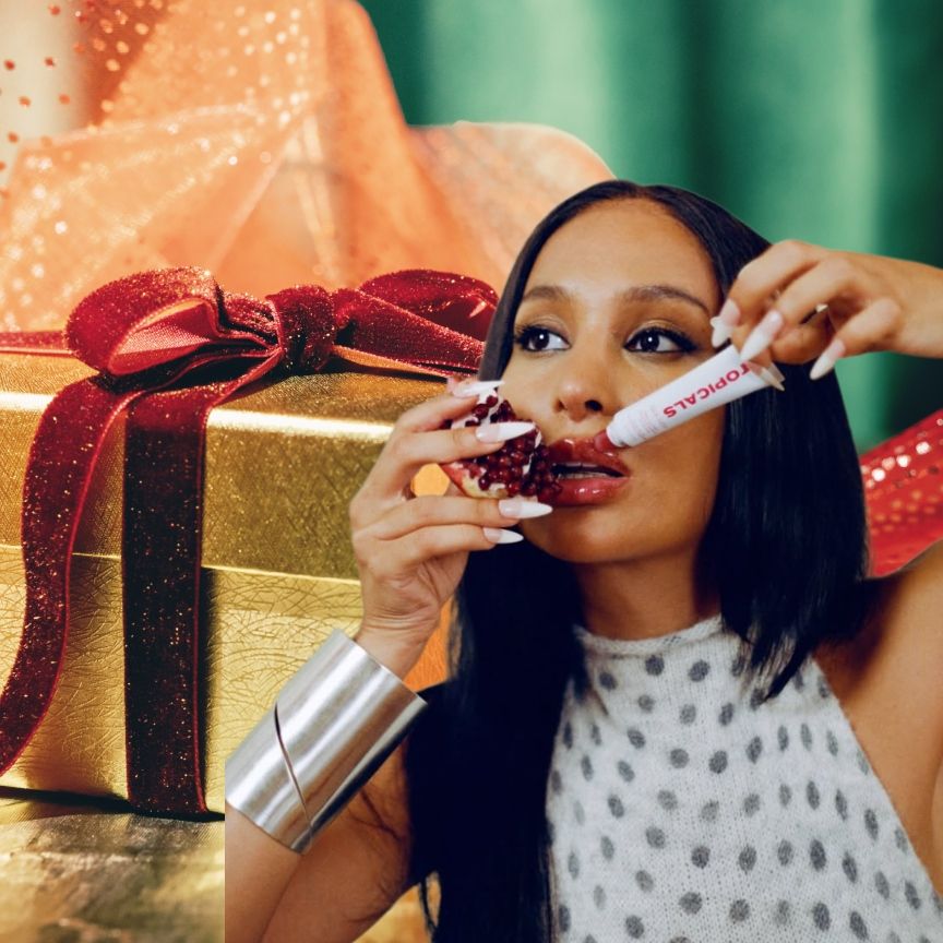 a golden gift package with a red ribbon next to a woman with dark hair and silver jewelry