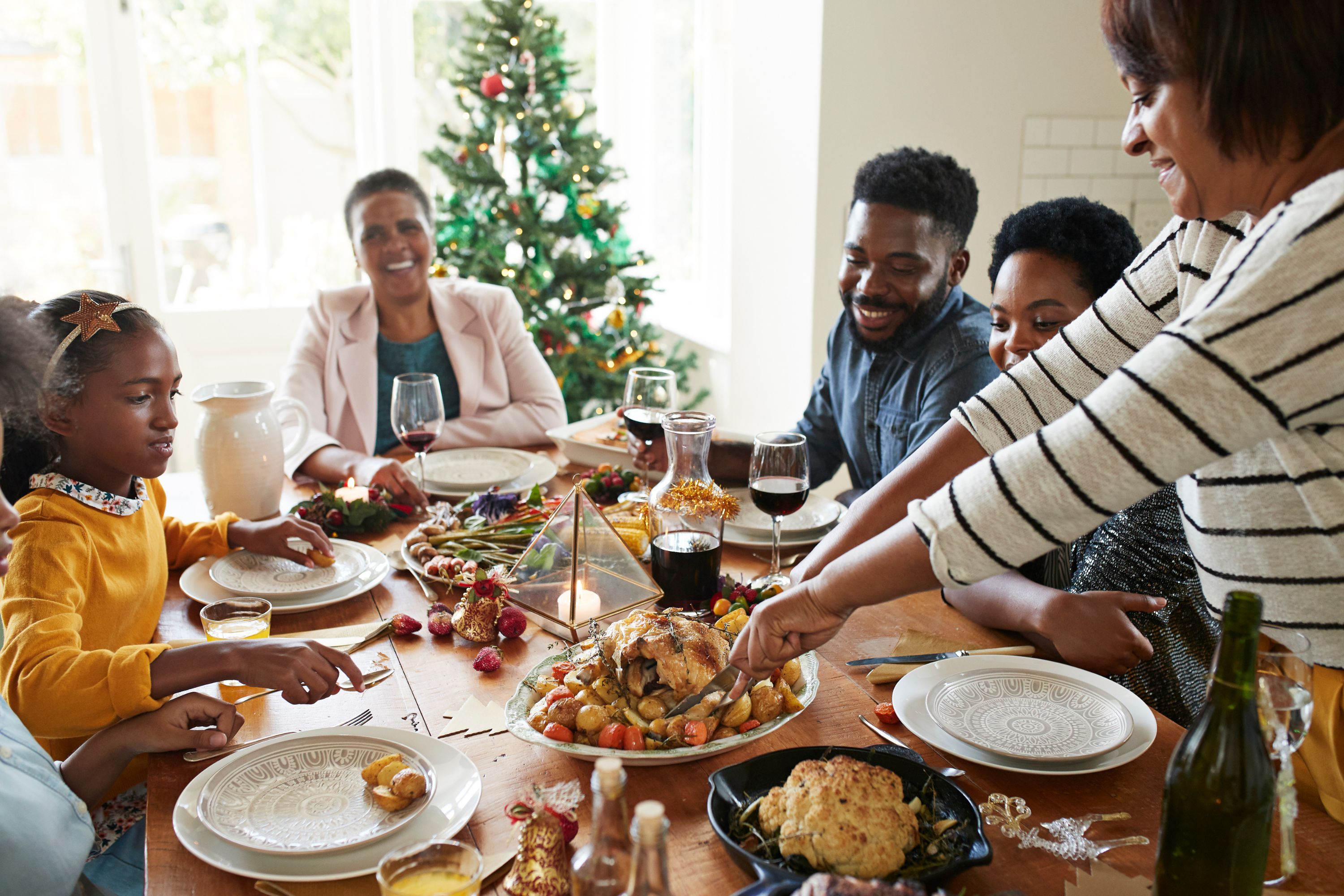 A family sitting around a table for Christmas dinner while a woman carves a turkey