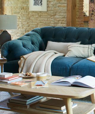 A living room with a dark blue couch with a white throw and pillows and a wooden coffee table with books and mugs on top of it