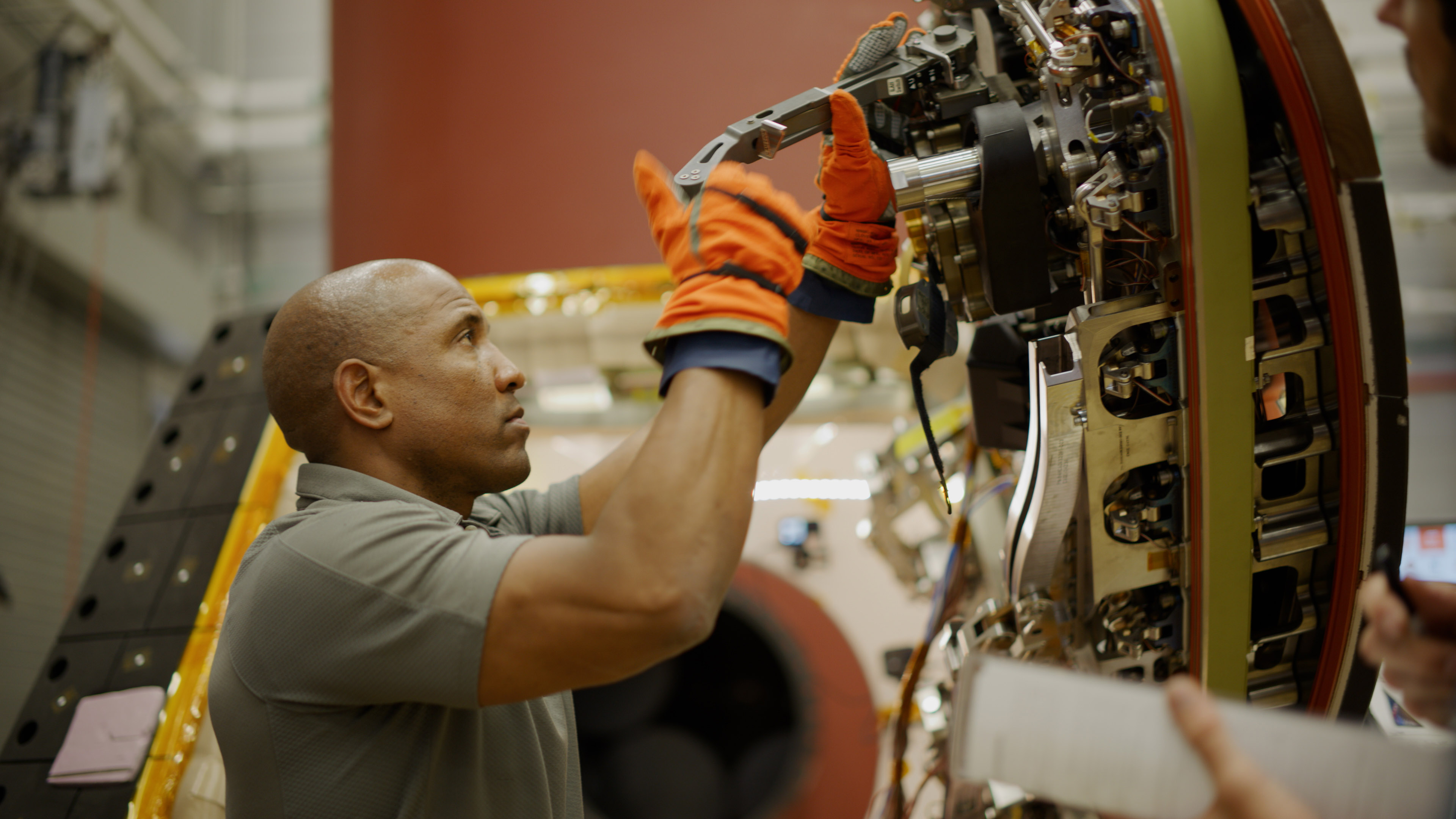 victor glover facing an open spacecraft hatch and using a tool on the door