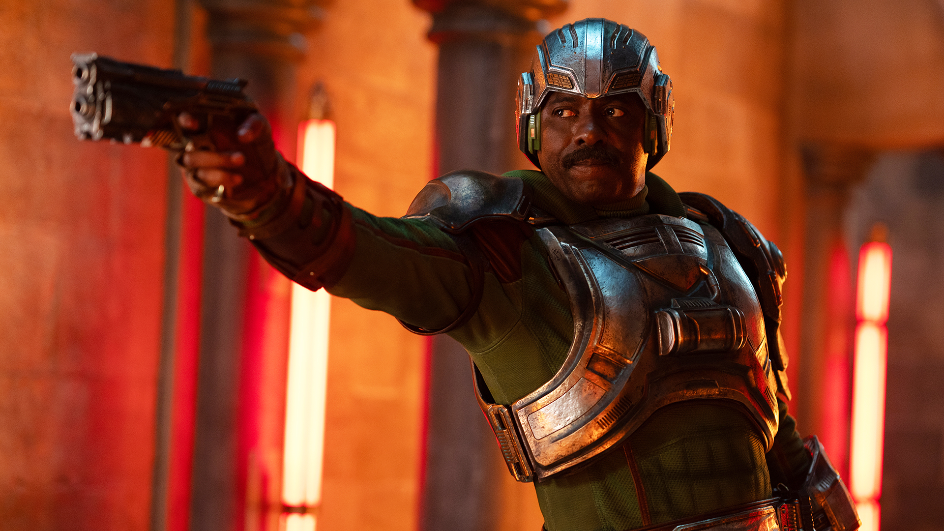 Idris Elba's Duncan/Man-at-Arms pointing a sidearm at someone standing off-camera in 2026's Masters of the Universe film