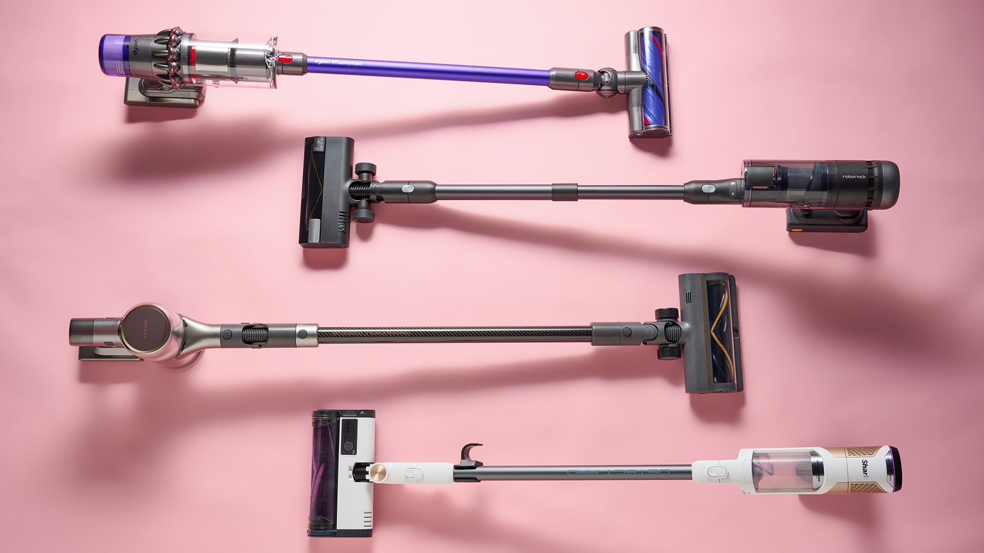 Four cordless vacuums, from Dyson, Roborock, Dreame and Shark, photographed against a pink background