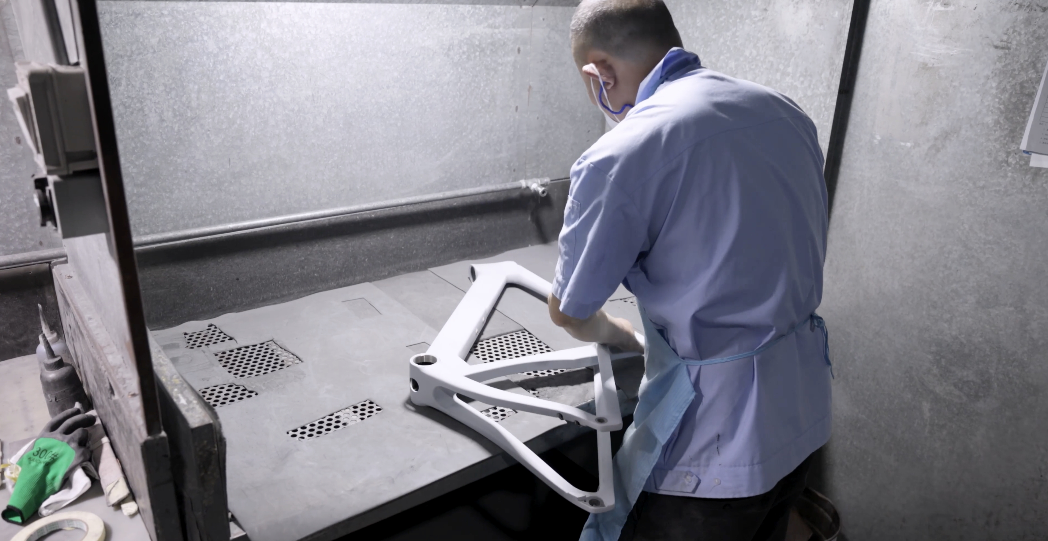A bare carbon frame being prepped by a worker in a blue shirt on a grey table