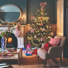 A living room decorated for Christmas with a bow-adorned tree in the corner and a decorated striped chair next to it 