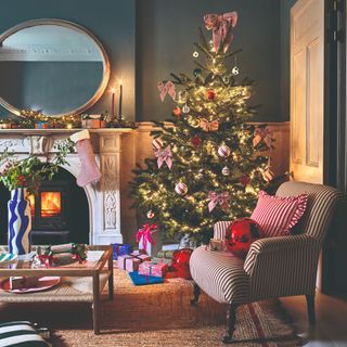 A living room decorated for Christmas with a bow-adorned tree in the corner and a decorated striped chair next to it