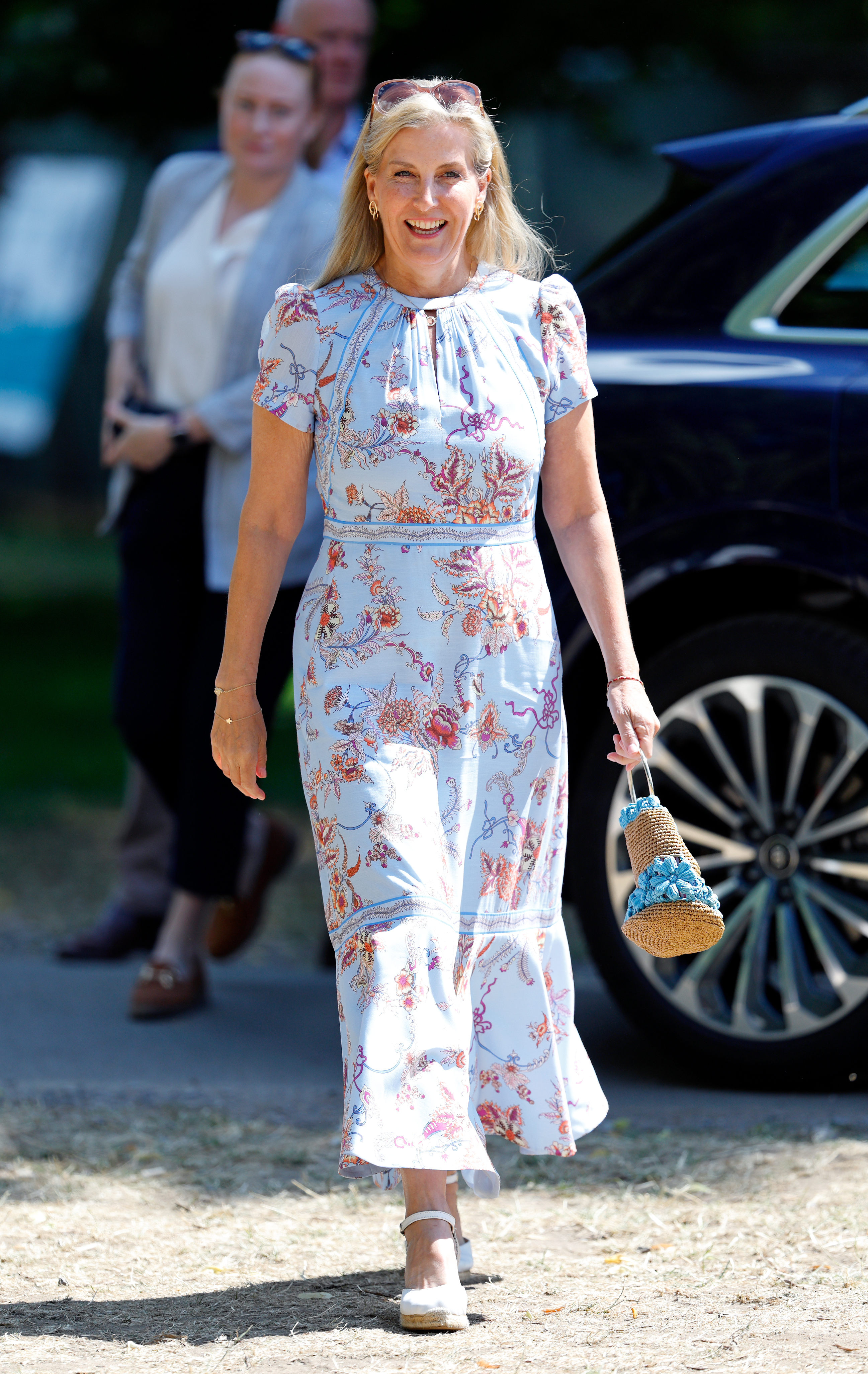 Duchess Sophie wearing a pale blue floral dress walking and smiling in a parking lot