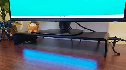 Razer Monitor Stand Chroma on desk with blue lighting reflecting off surface and Alienware gaming monitor on top.