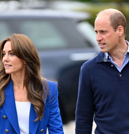 Kate Middleton wearing a blue blazer walking next to Prince William, dressed in a blue sweater, in front of a car and both looking to the left