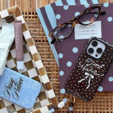 A dark brown white polka dot phone case and a sky-blue bow-patterned phone case from Skinnydip, on an aesthetic spread with matching notebooks and accessories.