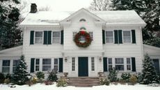 A large white house at Christmas with big wreath and snow