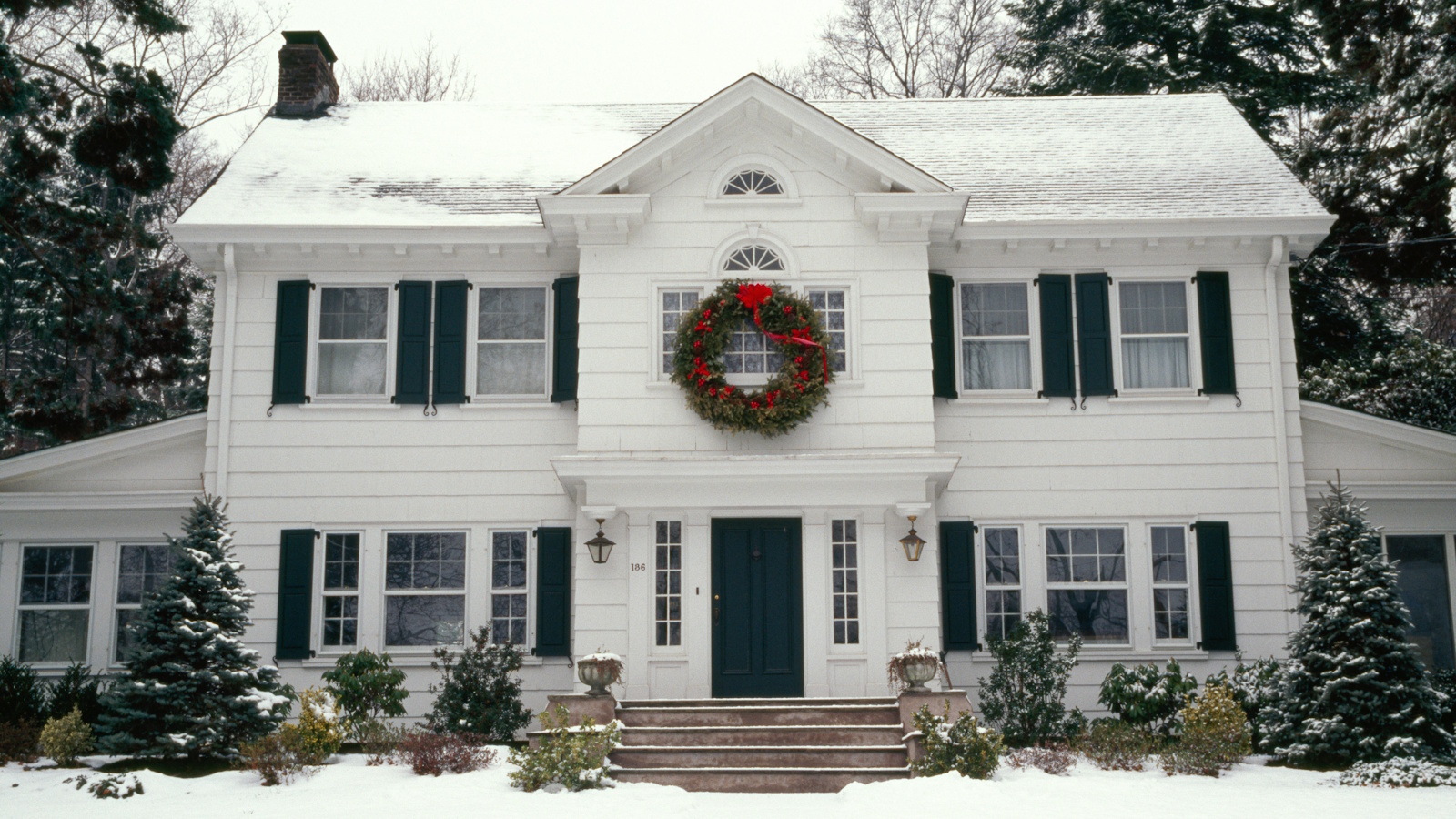 A large white house at Christmas with big wreath and snow