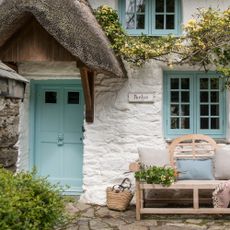 white cottage with blue door blue window wooden bench with cushion and plant