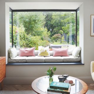 Bay window made into a window seat with grey cushions and smaller decorative cushions