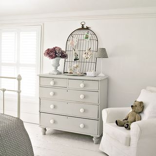 white wall with teddy bear on chair and chest of drawers