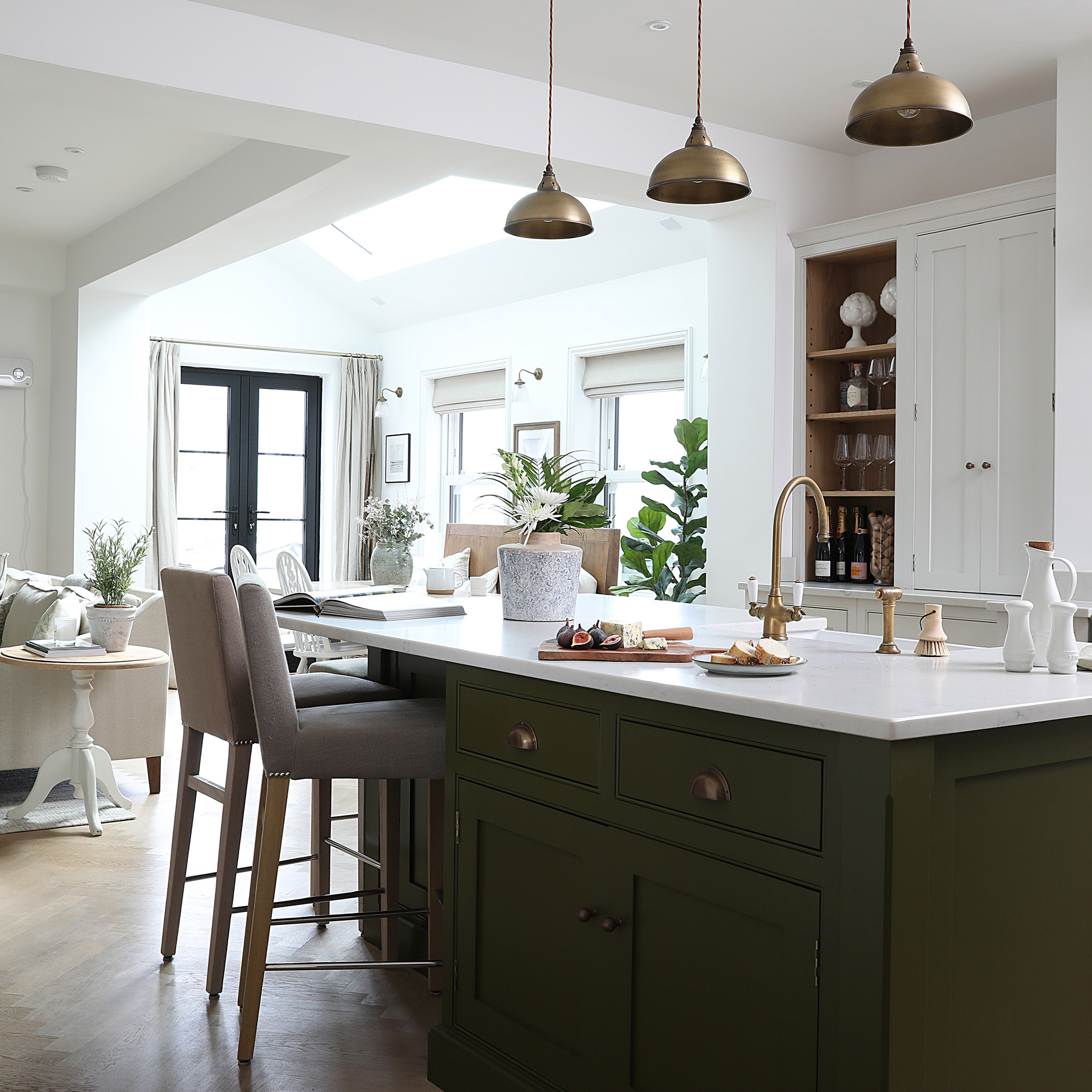  kitchen-diner in neutral extension with white walls black framed patio doors a green kitchen island with brass pendant lights and bar stools