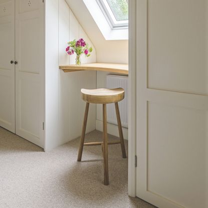 Wardrobes in a loft room next to a Velux window, with a shelf and a stool under the window