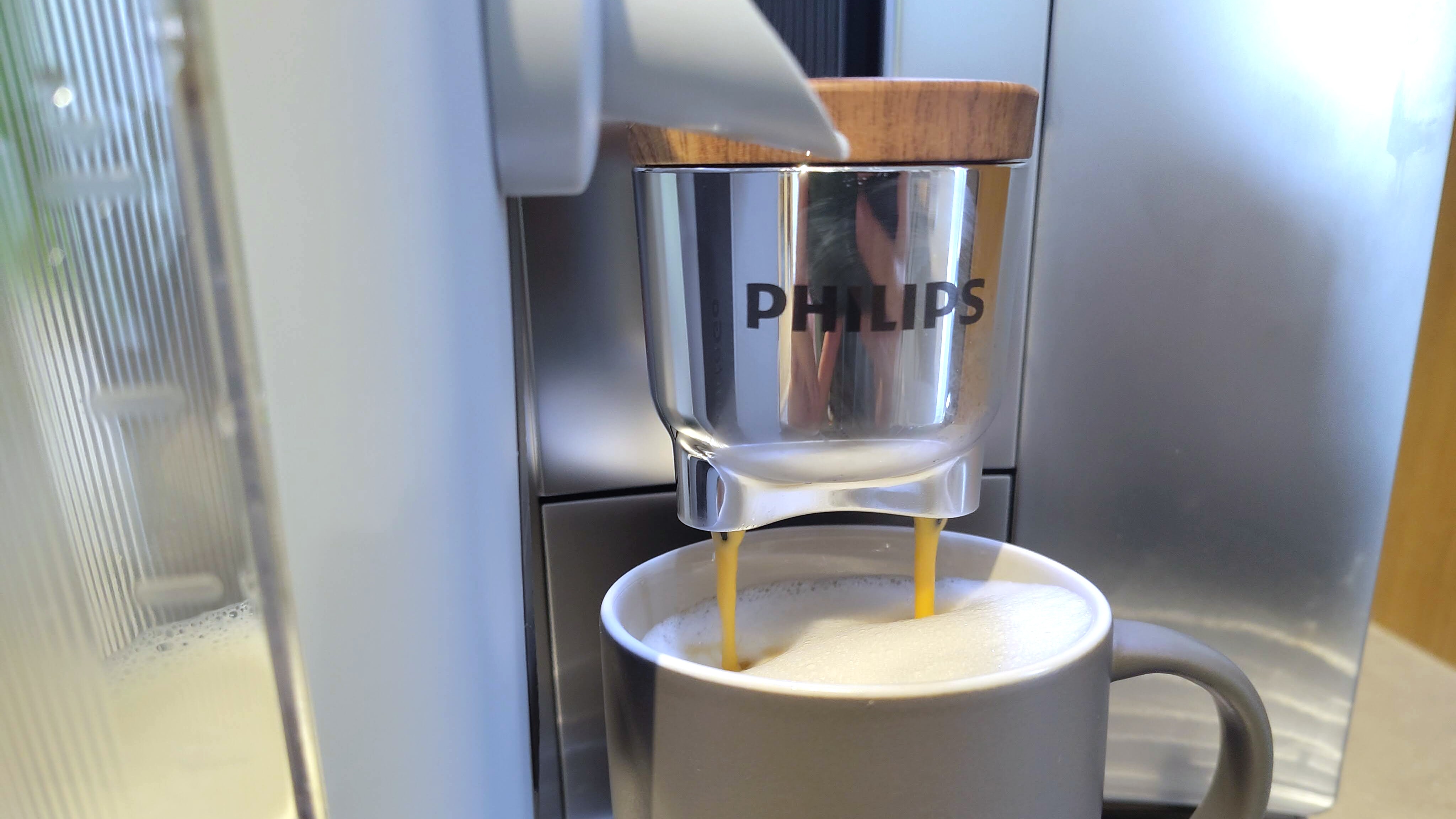 Philips Caf&amp;eacute; Aromis coffee maker dispensing espresso into latte
