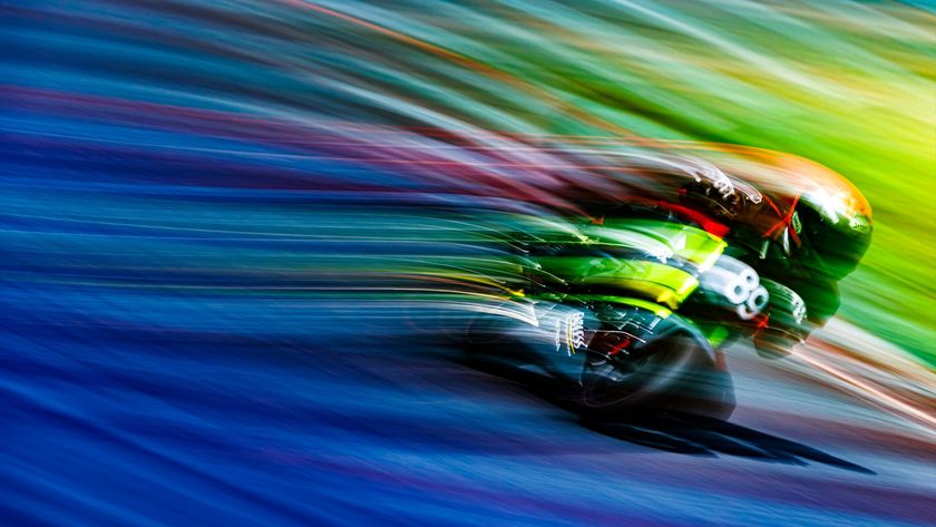A blurred, high-speed image of a race car, with a rainbow-like streaking of colors in the background, gives the impression of extreme motion.
