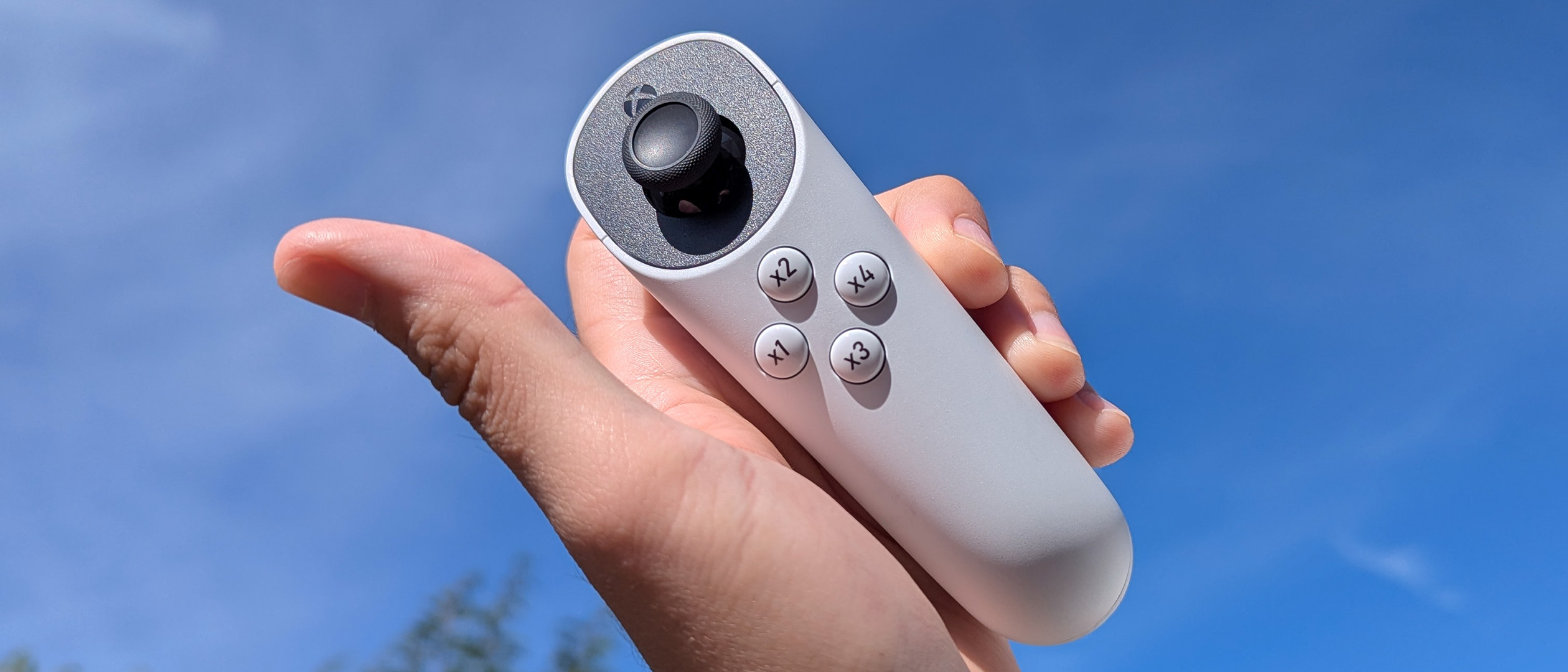 Xbox Adaptive Joystick held in hand, up to a blue cloudy sky