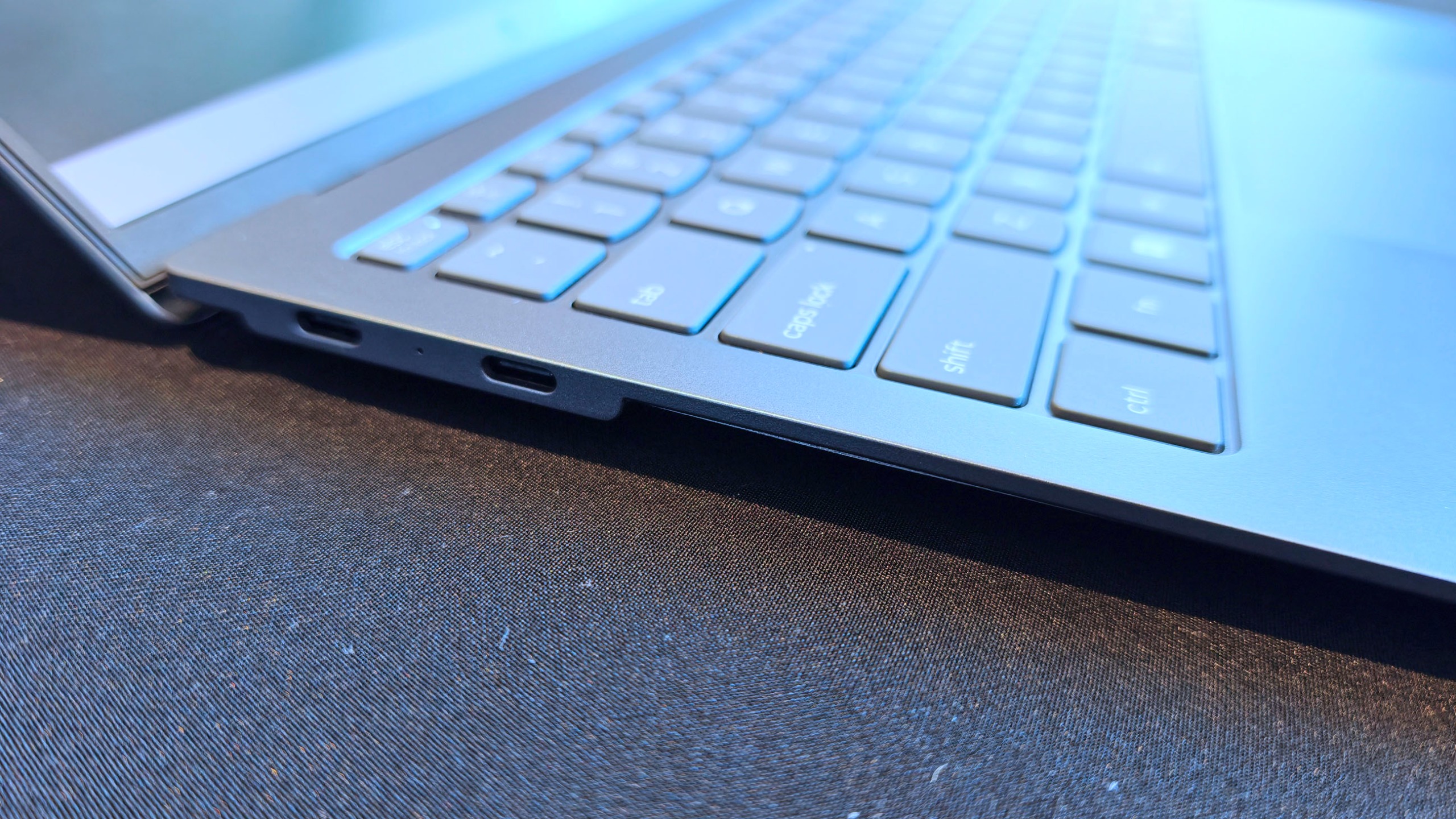 Angled close-up of the left side profile of a thin grey laptop, showing two USB-C ports along the slim edge.