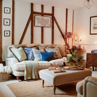 a cosy sofa covered in cushions and throws in a snug living room with wooden beamed walls and lit candles