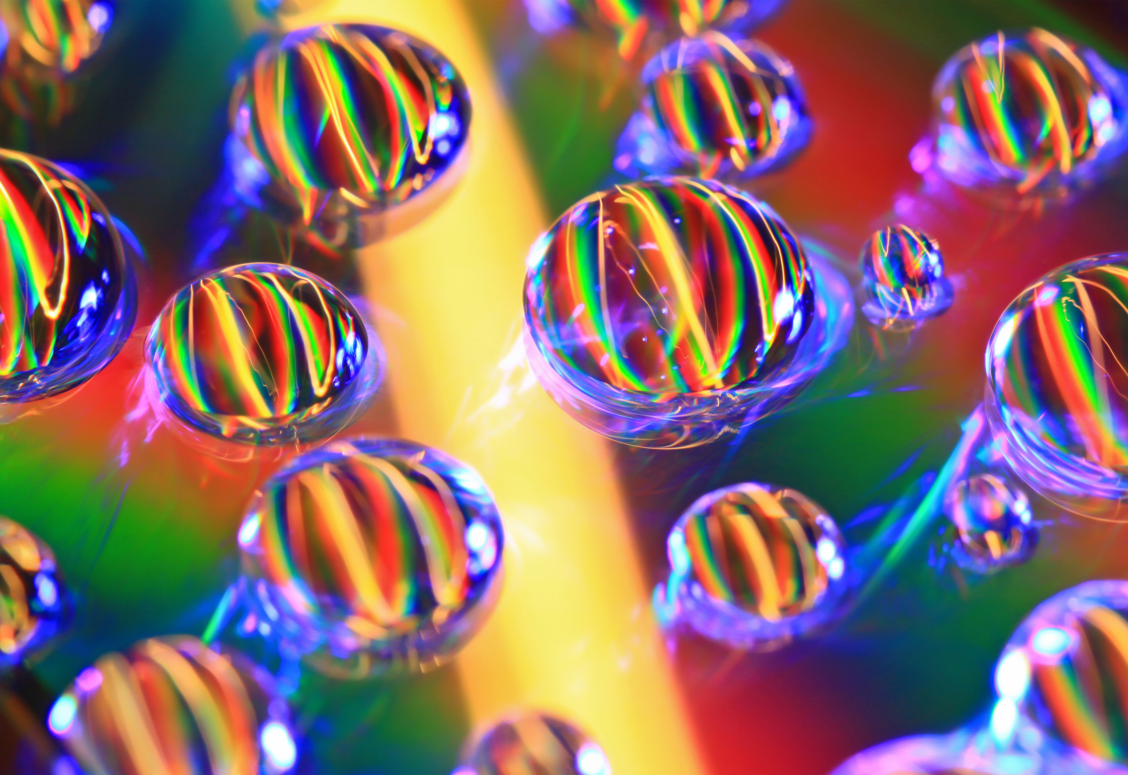 Close-up of water droplets on a colorful, iridescent surface, refracting light into vibrant rainbow patterns