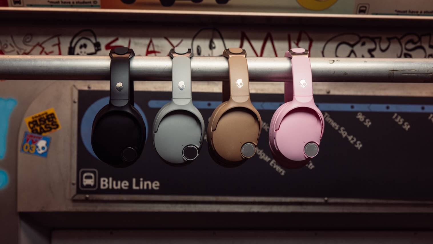 Four different color models of Skullcandy Crusher 1080, hung up on a bar in a metro.