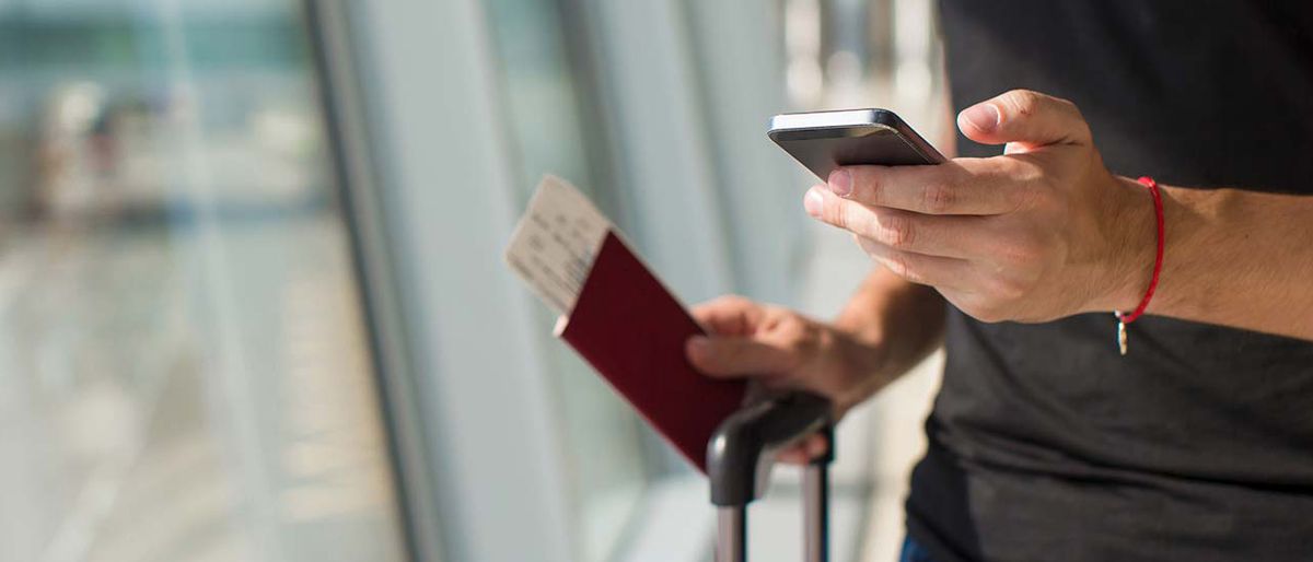 Man at airport terminal holding passport, ticket and phone