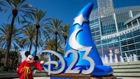 Mickey Mouse, dressed in his Sorcerer&rsquo;s Apprentice costume from Fantasia, poses beside a giant blue sorcerer&rsquo;s hat sculpture with a sparkling D23 logo outside the Anaheim Convention Center