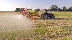 A tractor pulls a machine that sprays crops on a farm.