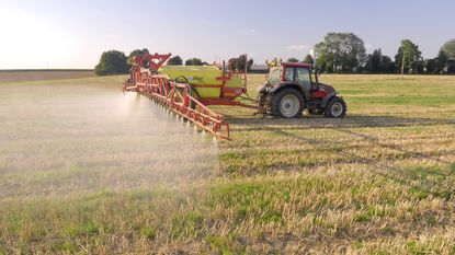 A tractor pulls a machine that sprays crops on a farm.