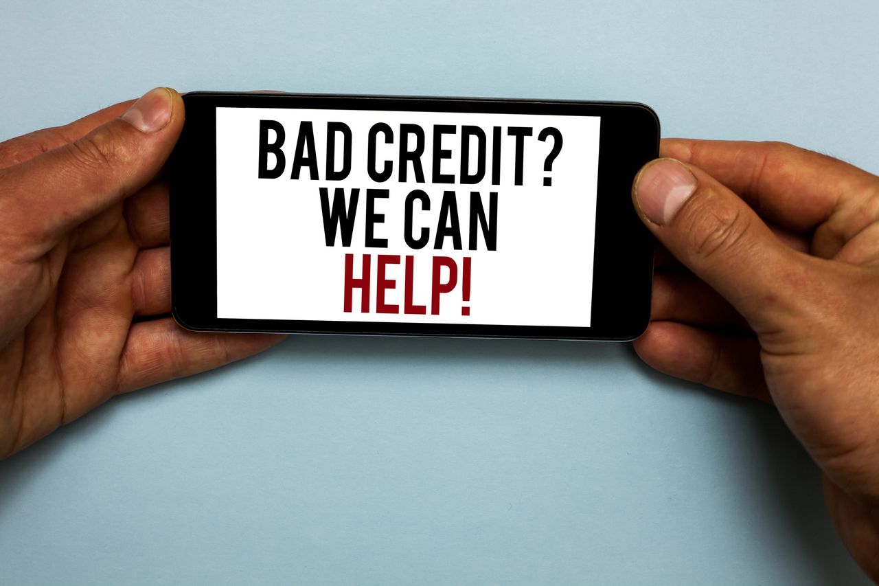 A man&#039;s hands holding a cell phone with the words &quot;Bad credit? We can hellp!&quot; on the screen.