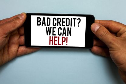A man's hands holding a cell phone with the words "Bad credit? We can hellp!" on the screen.