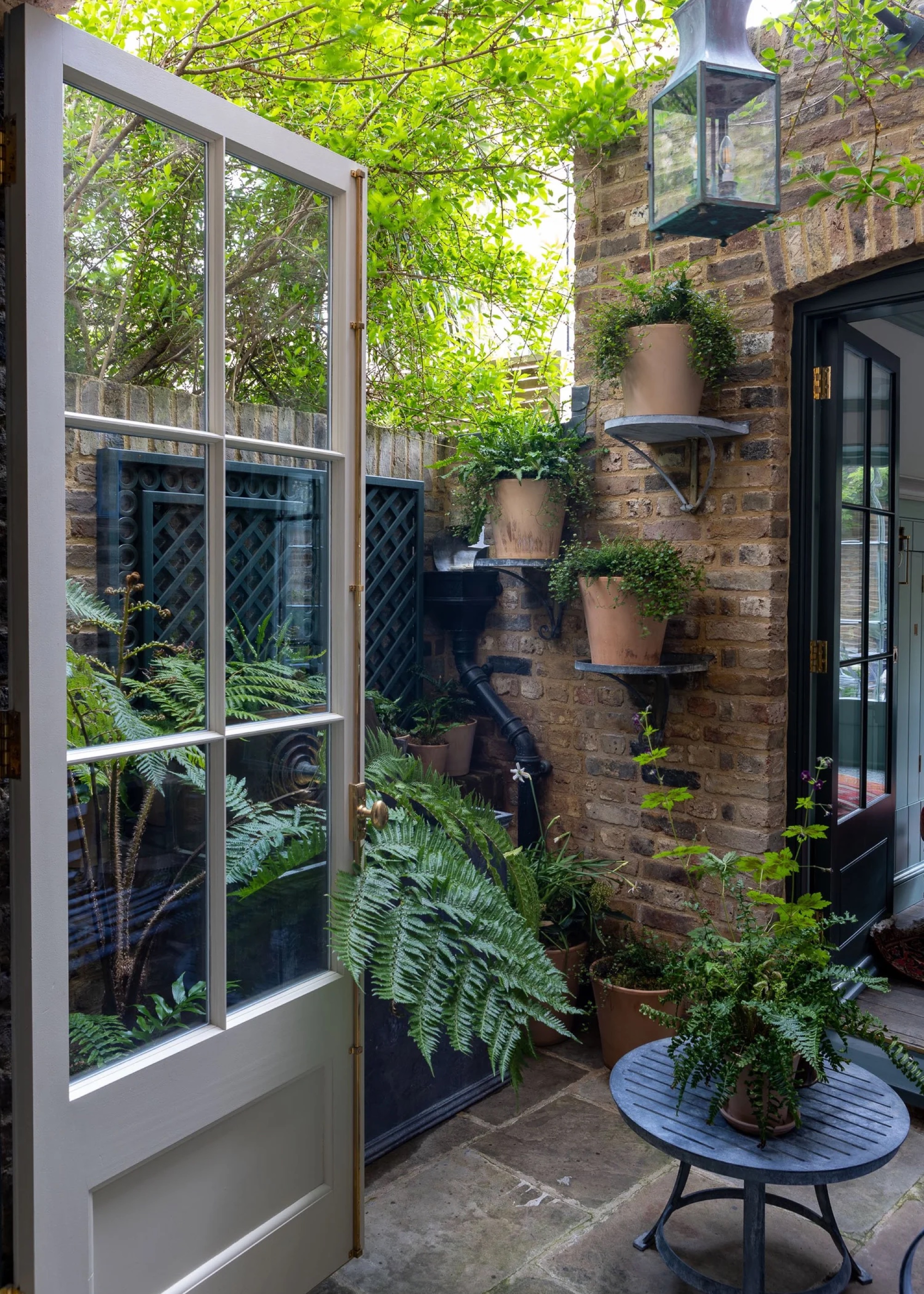 Small courtyard garden with vertical terracotta pots hung shelving on the wall