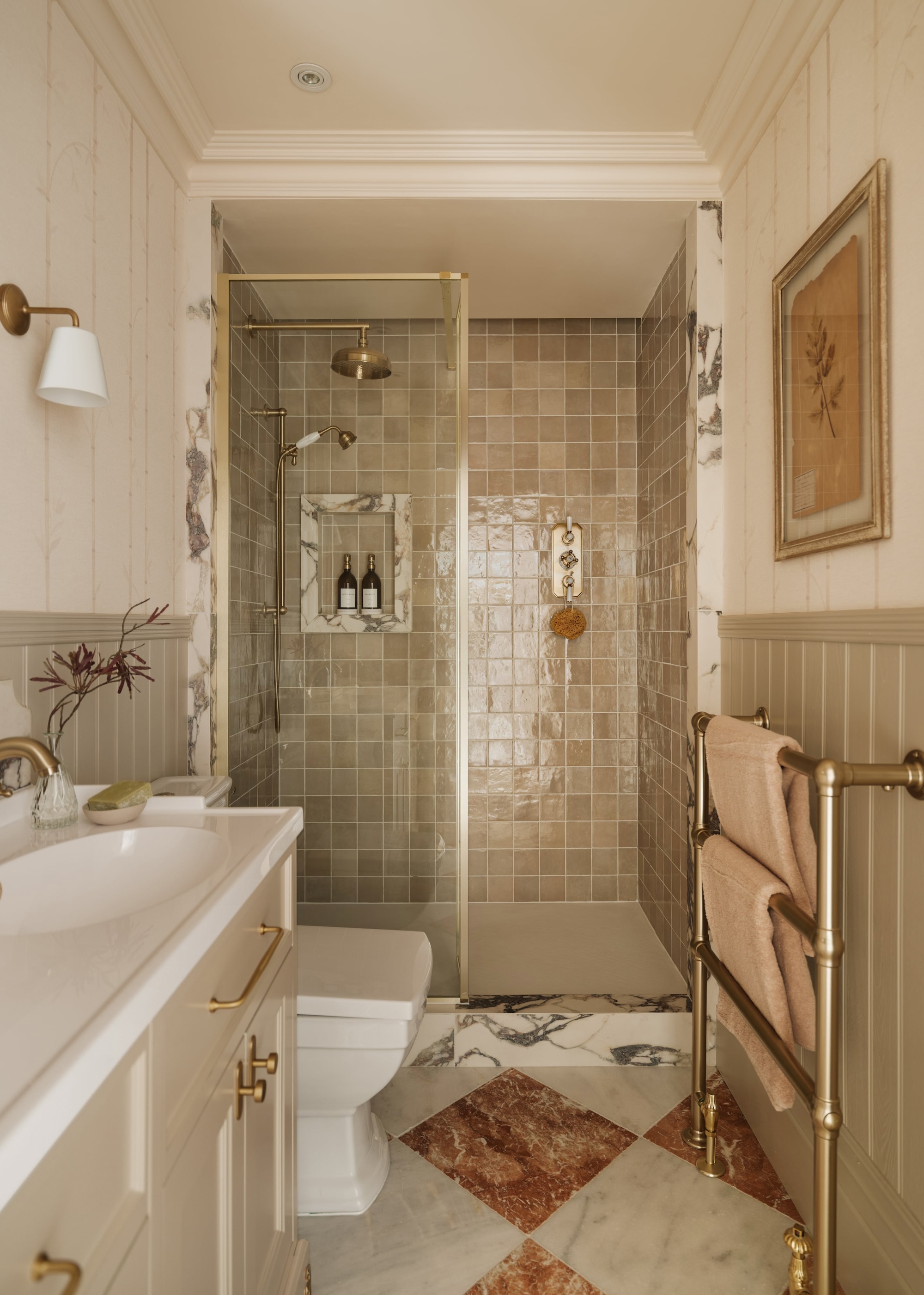 A compact bathroom in muted tones shown with tongue and groove panelling, marble checkerboard floors and a shower clad in zellige gloss ceramic tiles